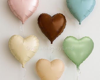 May include: Six heart-shaped balloons in various colors, including pink, blue, brown, beige, and green. The balloons are tied together with strings.