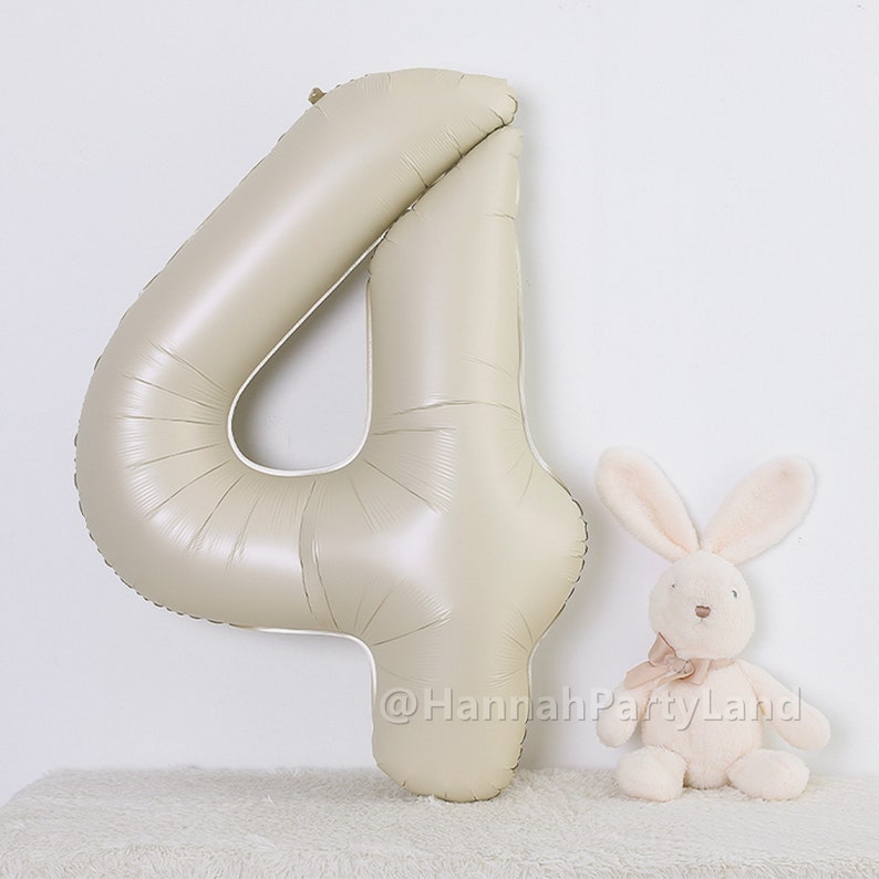 May include: A large, beige, foil number four balloon. A small, white, plush bunny with a pink bow is sitting in front of the balloon.