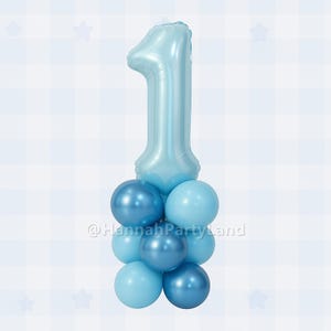 May include: A large light blue number one balloon with a cluster of smaller blue balloons underneath. The balloons are arranged in a pyramid shape. The text "@HannahPartyLand" is visible in the image.