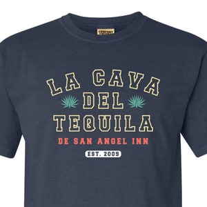 May include: Navy blue t-shirt with the text "LA CAVA DEL TEQUILA" in a vintage font. Below the text is "DE SAN ANGEL INN" and "EST. 2009". The shirt has a crew neck and short sleeves.