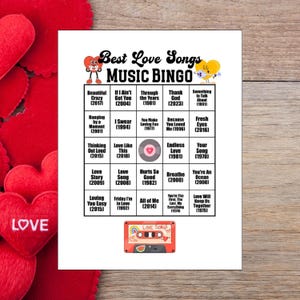 May include: A white sheet of paper with a "Best Love Songs Music Bingo" game. The bingo card features song titles and years, with a red cassette tape graphic at the bottom. Red heart decorations are in the background.