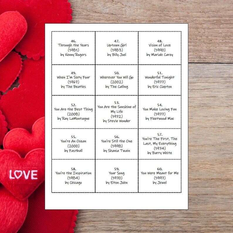 May include: A white printed sheet with song titles and artists, including "Uptown Girl" by Billy Joel and "You're Still the One" by Shania Twain. The sheet is on a wooden surface, with red heart-shaped decorations in the background.