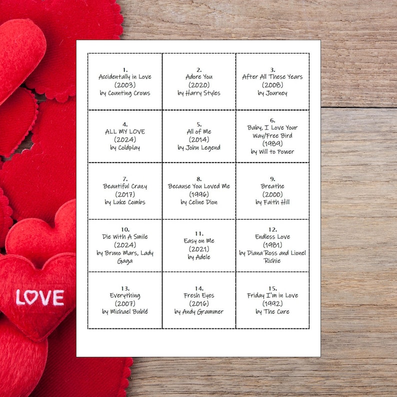 May include: A white card with fifteen song titles and artist names, arranged in a grid. The songs include "Accidentally in Love," "Adore You," and "After All These Years." The card is on a wooden surface, with red heart decorations in the background.