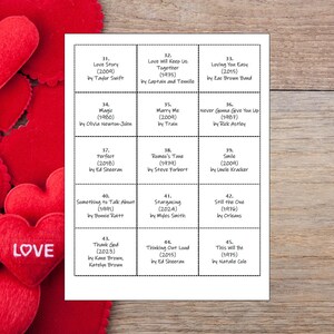 May include: A white printed sheet with song titles and artists, including "Love Story" by Taylor Swift and "Perfect" by Ed Sheeran. Red heart-shaped decorations with the word "LOVE" are in the background. The sheet is on a wooden surface.