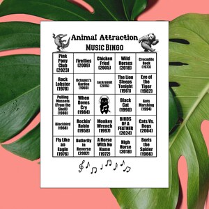 K&ouml;nnte beinhalten: Eine wei&szlig;e Bingo-Karte mit dem Titel "Animal Attraction MUSIC BINGO" mit tierischen Songtiteln und Jahreszahlen. Enth&auml;lt Illustrationen eines Alligators und eines B&auml;ren. Die Karte befindet sich vor einem rosa Hintergrund mit einem gr&uuml;nen Blatt.