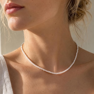 May include: A delicate necklace composed of a single strand of small, white, round freshwater pearls. The pearls are uniform in size and shape, strung closely together to form a continuous, smooth, and circular chain that rests around the neck.