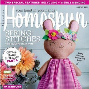 Könnte beinhalten: Homespun Magazin-Cover mit einem rosa-weiß karierten Kleid auf einem braunen Hasen mit einer Blumenkrone. Der Titel des Magazins lautet "Homespun" und der Text auf dem Cover lautet "Spring Stitches" und "Festive Stitchery".