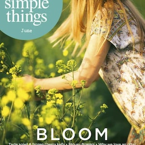 May include: Magazine cover featuring the text "the simple things" and "June" in white on a teal circle. The word "BLOOM" is in large white letters. A person is in a field of yellow flowers, wearing a floral print top and a straw hat.