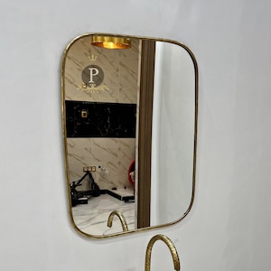 May include: A white marble oval sink with a gold faucet and a gold framed mirror above it. The mirror is reflecting a room with a gold light fixture.