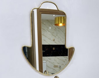May include: A white marble oval sink with gold faucet and a gold hamsa mirror on the wall behind it.