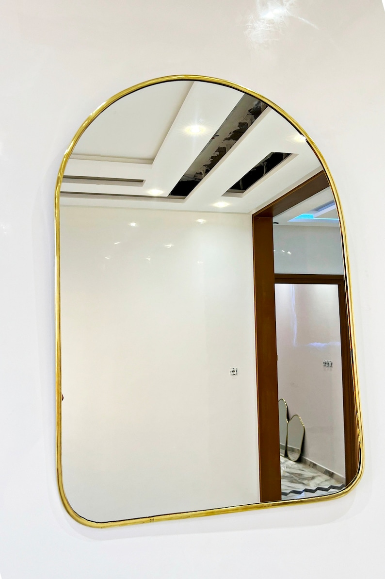 Puede incluir: Un espejo arqueado con marco dorado refleja un techo blanco con iluminaci&oacute;n empotrada y una puerta que conduce a otra habitaci&oacute;n.