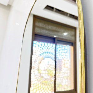 Puede incluir: Un espejo arqueado con marco dorado, que refleja una ventana con un dise&ntilde;o estampado.