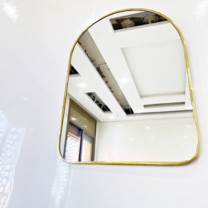 Puede incluir: Un espejo arqueado con marco dorado, reflejando un techo blanco con vigas a la vista.