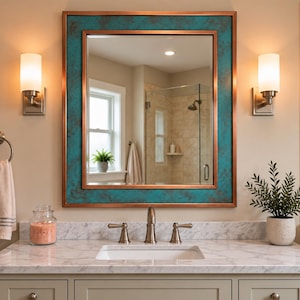 Può includere: Uno specchio da parete rettangolare con cornice color rame e inserto testurizzato color ottanio. Lo specchio è montato sopra un piano lavabo in marmo bianco con lavandino centrale, affiancato da due lampade da parete con paralumi in vetro satinato.