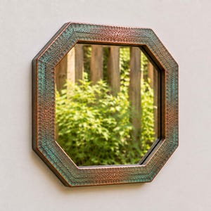 May include: An octagonal wall mirror featuring a textured, hammered metal frame with a dual-tone finish. The frame displays a blend of deep copper and oxidised teal green hues, creating a weathered appearance around the central reflective glass surface.