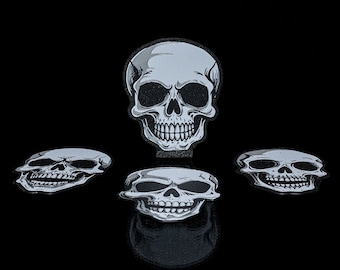 Pode incluir: Quatro desenhos de caveiras brancas sobre um fundo preto. As caveiras têm olhos pretos e um sorriso cheio de dentes.