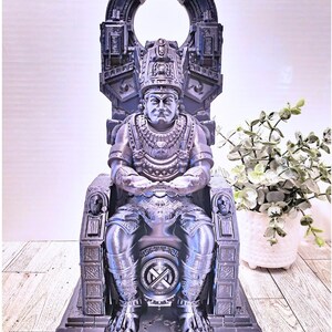May include: A detailed, gray, 3D printed statue of a figure sitting on a throne. The figure is wearing a crown and ornate clothing. The throne is decorated with intricate carvings.