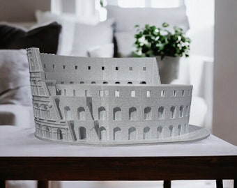 May include: A gray miniature model of the Colosseum, a famous Roman amphitheater, sits on a wooden table in a living room setting.