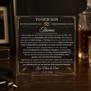 May include: A square, clear acrylic plaque featuring a black background with gold-colored decorative borders and text. The inscription reads: TO OUR SON ON YOUR WEDDING DAY FOREVER BEGINS TODAY, followed by a message to Thomas, dated 11.21.2026.