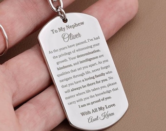 May include: Silver keychain with a dog tag charm engraved with a message to a nephew named Oliver. The message expresses pride in his growth and qualities. It reads "To My Nephew Oliver As the years have passed, I've had the privilege of witnessing your growth. Your determination, kindness, and intelligence are qualities that set you apart. As you navigate through life, never forget that you have a loving family who will always be there for you. No matter where life takes you, please carry with you the knowledge that I am so proud of you. With All My Love Aunt Karen"