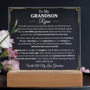 Puede incluir: Una placa acrílica enmarcada con un borde dorado y un mensaje sincero para un nieto llamado Ryan. El mensaje expresa amor, orgullo y apoyo. Dice: "A mi nieto Ryan, Desde el momento en que llegaste a mi vida, llenaste mi corazón con un amor más profundo que las palabras pueden expresar. Verte crecer y convertirte en la persona increíble que eres hoy ha sido una de mis mayores alegrías, y estoy tan orgulloso de ti en todos los sentidos. No importa a dónde te lleve la vida, recuerda siempre que estoy aquí para ti, animándote, apoyándote y amándote incondicionalmente. Eres un nieto increíble, y me siento tan bendecido de tenerte en mi vida. Gracias por la alegría, la risa y el amor que traes a mi mundo. Eres un verdadero regalo, y atesoro cada momento que compartimos. Puede que no esté aquí para el resto de tu vida, pero te prometo que te amaré por el resto de la mía. Tengo muchas ganas de ver todas las cosas increíbles que el futuro te depara. Con todo mi amor, Abuela."