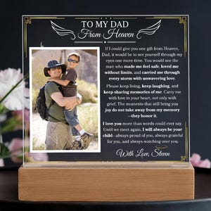 Puede incluir: Placa conmemorativa con una foto de un padre y un hijo, colocada sobre una base de madera. El texto dice "A mi papá del cielo" con un mensaje sincero y el nombre "Steven" en la parte inferior. La placa es transparente con un fondo negro.