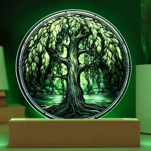 May include: A stained glass lamp with a green willow tree design. The lamp is illuminated with a green light and sits on a wooden base.