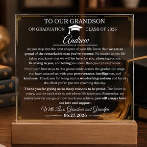 May include: A clear acrylic graduation plaque with a wooden base. The plaque features gold lettering that reads "To Our Grandson" and a personalized message. A graduation cap graphic is at the top. The date 06.27.2026 is at the bottom.