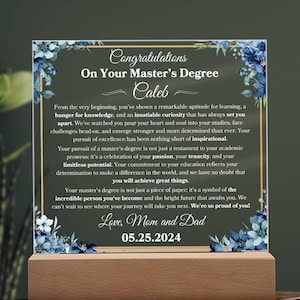May include: A blue and white floral design on a clear acrylic plaque with a wooden base. The plaque has a gold border and the text "Congratulations on Your Master's Degree Caleb" and a message from Mom and Dad.