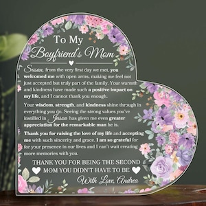 May include: A heart-shaped acrylic plaque with a floral design and a message to a boyfriend's mom. The message reads "To My Boyfriend's Mom Susan, from the very first day we met, you welcomed me with open arms, making me feel not just accepted but truly part of the family. Your warmth and kindness have made such a positive impact on my life, and I cannot thank you enough. Your wisdom, strength, and kindness shine through in everything you do. Seeing the strong values you've instilled in Jason has given me even greater appreciation for the remarkable man he is. Thank you for raising the love of my life and accepting me with such sincerity and grace. I am so grateful for your presence in our lives and I can't wait creating more memories with you. THANK YOU FOR BEING THE SECOND MOM YOU DIDN'T HAVE TO BE With Love, Andrea"