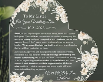 May include: A heart-shaped acrylic plaque with a floral design and the text "To My Sister On Your Wedding Day 10.21.2023". The text continues with a heartfelt message to the sister on her wedding day, ending with "With All My Love, Sabrina".