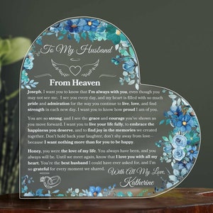 Può includere: Una placca acrilica a forma di cuore con un design floreale e il testo "To My Husband From Heaven". La placca presenta un messaggio d'amore e ricordo, che termina con "With All My Love, Katherine".