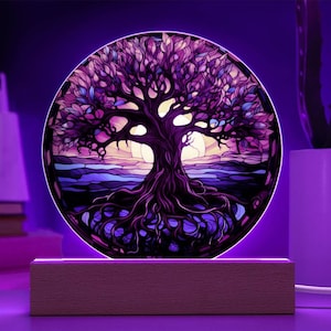 Könnte beinhalten: Ein lila und blauer Glasmalereibaum des Lebens mit filigranen Details, beleuchtet von einer Lichtbasis. Der Baum ist von einem runden Rahmen umgeben und hat einen Sonnenuntergangs-Hintergrund.