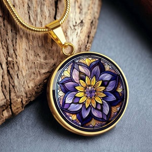 Puede incluir: Un collar de cadena dorada con un colgante redondo que presenta un diseño de mandala colorido con tonos morados, amarillos y rosados. El mandala es intrincado y detallado, con un patrón floral.