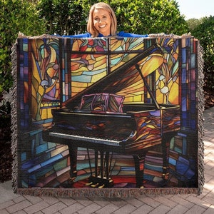 May include: A tapestry throw blanket featuring a stained glass style image of a grand piano in a room with a large window. The piano is black with gold accents and the stained glass is in shades of blue, yellow, red, and green.