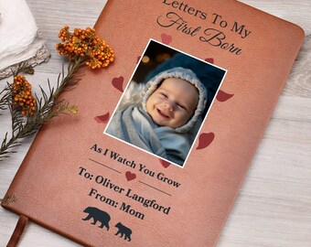 May include: A brown leather journal with the text "Letters To My First Born" and a photo of a baby. The journal also includes the text "As I Watch You Grow" and "To: Oliver Langford From: Mom". Decorative hearts and bear silhouettes are also present.