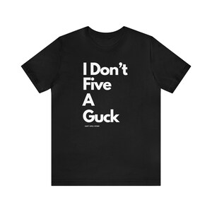 May include: Black t-shirt with white text that reads "I Don't Five A Guck" and the smaller text "Can't Spell Either".