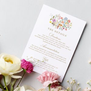 May include: A white wedding invitation card with gold lettering and a watercolor floral design. The card includes details about the wedding ceremony, including directions, accommodation, and gifts.