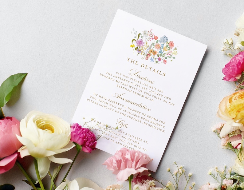 May include: A white wedding invitation card with gold lettering and a watercolor floral design. The card includes details about the wedding ceremony, including directions, accommodation, and gifts.