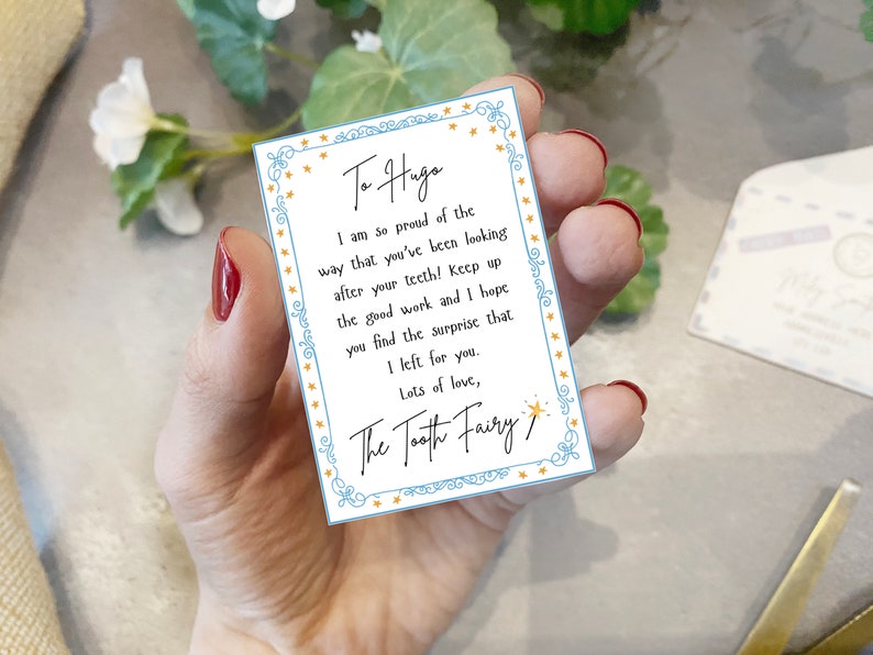 May include: A blue and white card with gold stars around the border. The card has a message for "Haga" from the Tooth Fairy. The message says, "I am so proud of the way that you've been looking after your teeth! Keep up the good work and I hope you find the surprise that I left for you. Lots of love, The Tooth Fairy."