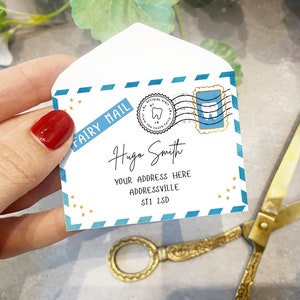May include: A white envelope with a blue and gold design. The envelope has a stamp with a tooth on it and the words "Fairy Mail" written on it. The envelope is addressed to "Hugo Smith" with an address below.