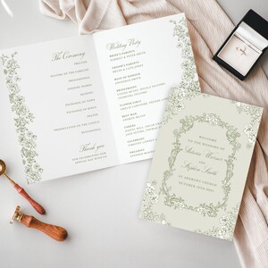 Op de afbeelding: Bruiloft briefpapier set met een trouwprogramma, uitnodiging en ringdoos. Het programma en de uitnodiging hebben bloemenranden. Een gouden ring zit in een zwarte doos. Een lakzegel en lepel zijn ook aanwezig.