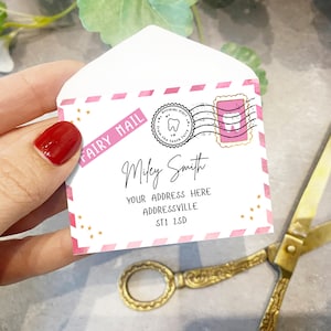 May include: A pink and white envelope with gold stars and the words "Fairy Mail" printed on it. The envelope is addressed to "Miley Smith" with an address and postcode. The envelope has a pink stamp with a tooth on it.