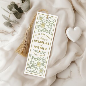 Può includere: Un segnalibro bianco con un nappa dorata, con un design floreale e il testo "Save the Date for the wedding of Annabelle and Matthew 01.01.2026". Il segnalibro ha un bordo dorato ed elementi decorativi.