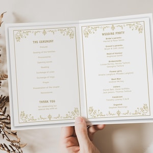 Op de afbeelding: Een trouwprogramma met gouden bloemaccenten en tekst. Het programma bevat de details van de ceremonie, de leden van het bruiloftsfeest en een bedankbericht. Het programma wordt in een hand gehouden.