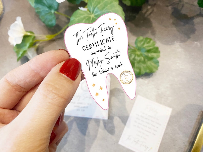 May include: A white tooth-shaped certificate with pink edges, gold stars, and the text "The Tooth Fairy Certificate awarded to Miley Smith for losing a tooth".