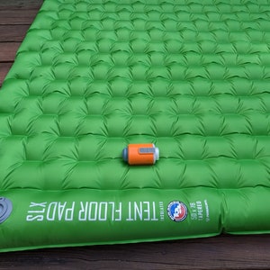 May include: Green inflatable tent floor pad with a gray valve and the text "TENT FLOOR PAD XLX" printed on the side. A small orange pump is on top of the pad.