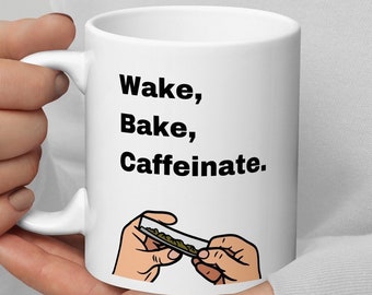 May include: White ceramic mug with a black graphic that says "Wake, Bake, Caffeinate." The graphic also includes a cartoon hand rolling a joint.