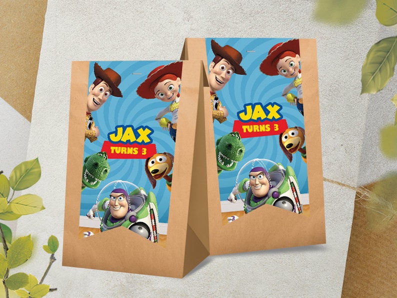 Puede incluir: Dos bolsas de regalo de papel marr&oacute;n con dise&ntilde;os de personajes de Toy Story. Las bolsas tienen etiquetas azules y blancas con el texto "Jax Turns 3".