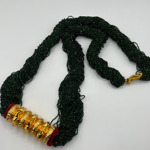 Peut inclure: Un collier de perles vert foncé avec des accents dorés. Le collier présente une série de perles dorées ornées et un fermoir doré. Les perles sont enfilées ensemble pour créer un long collier élégant.